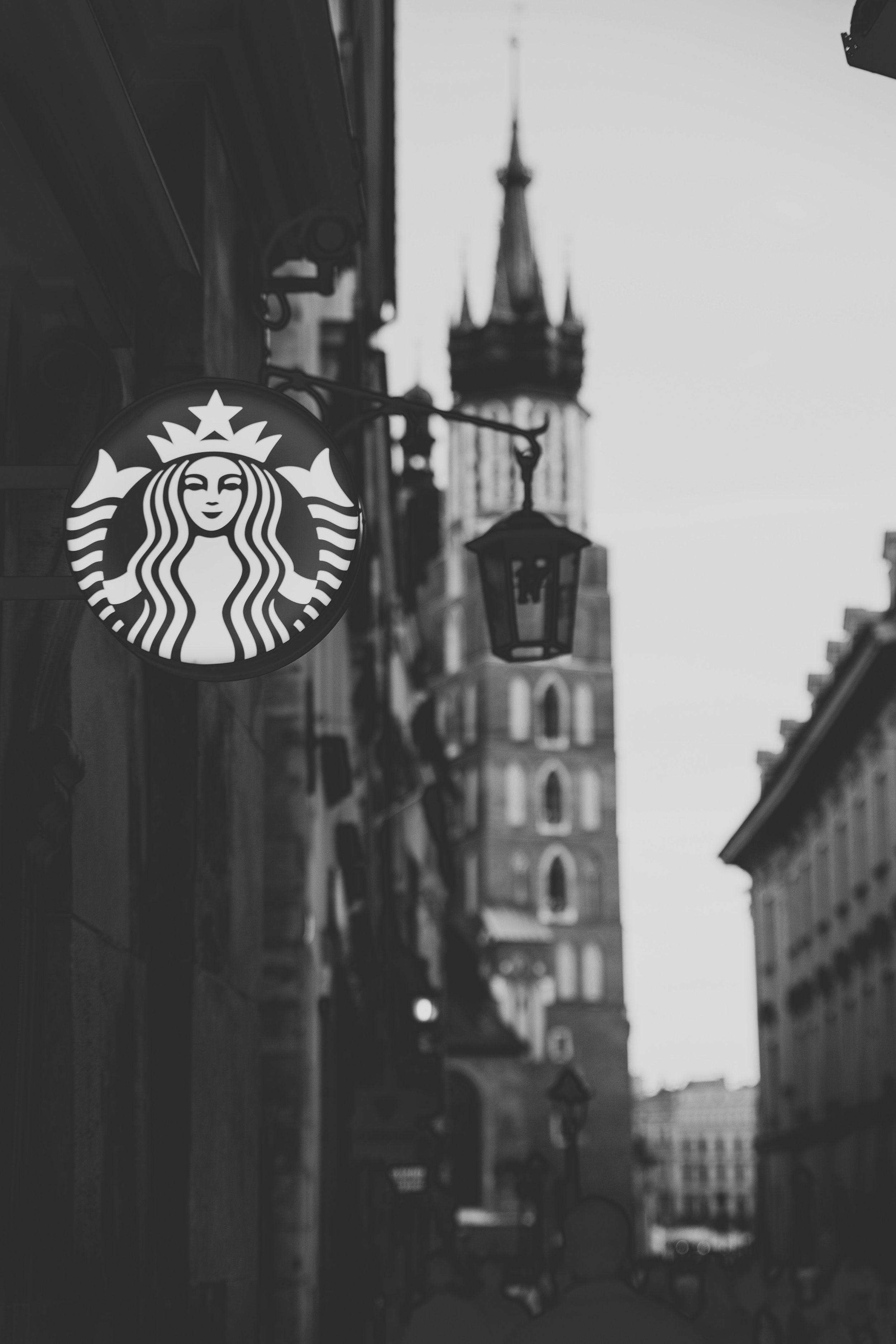 A Starbucks sign hangs in the foreground, with a medieval town out of focus behind
