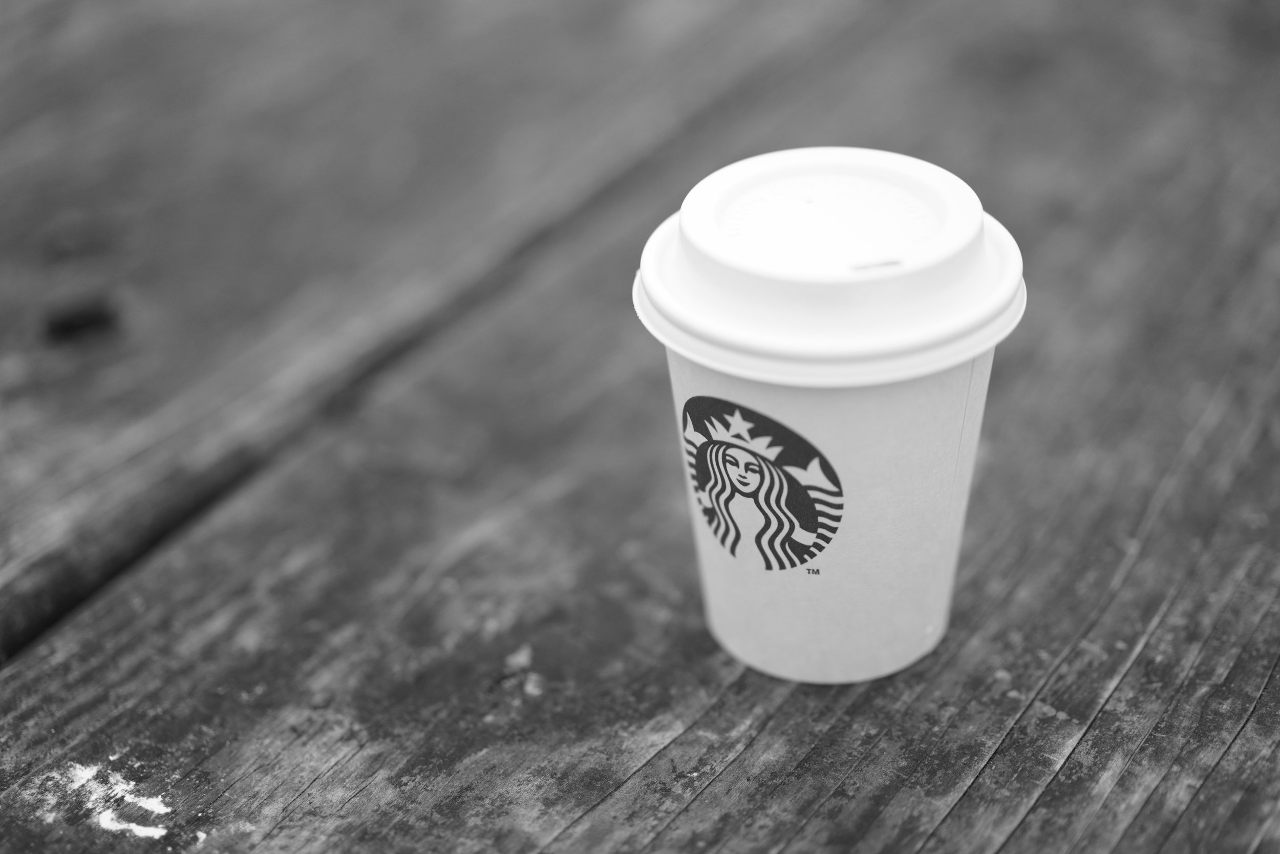A white Starbucks takeaway cup sits on a wooden outdoor table