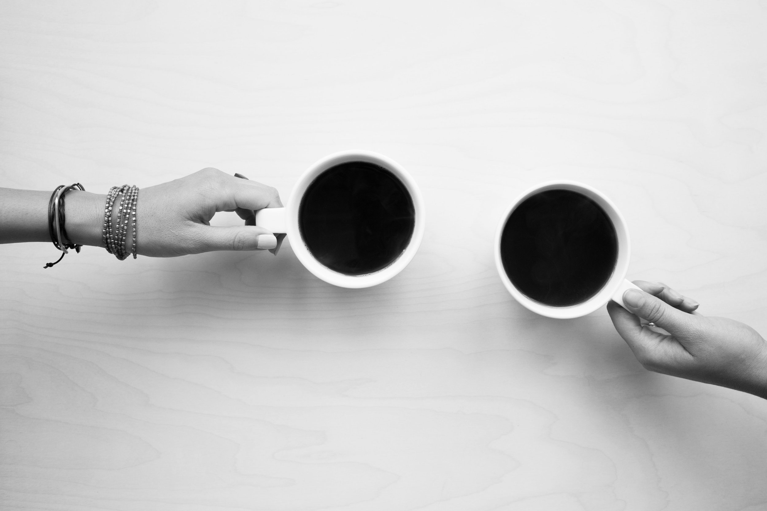 Two hands each hold a cup of coffee, seen from above