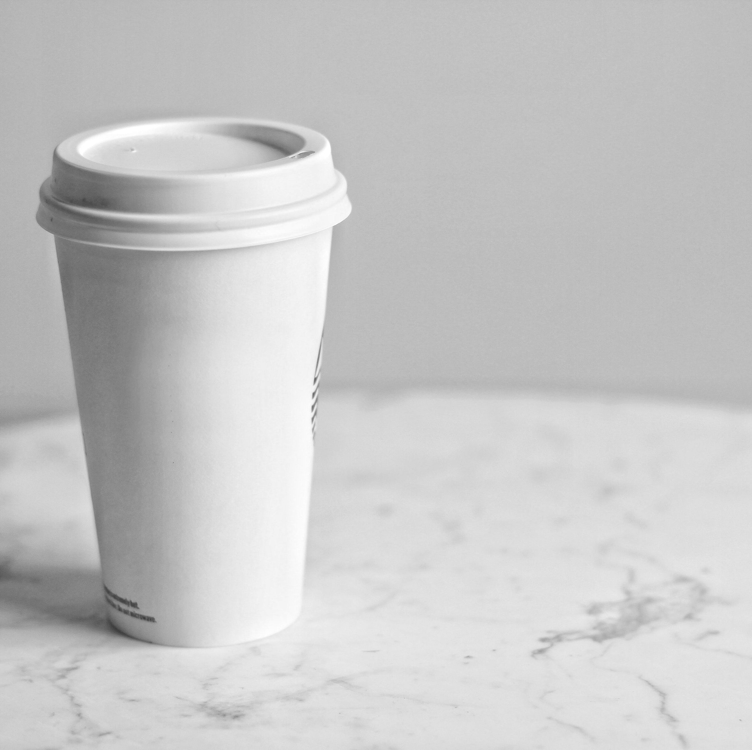 A white single-use coffee cup sits on a marble table.