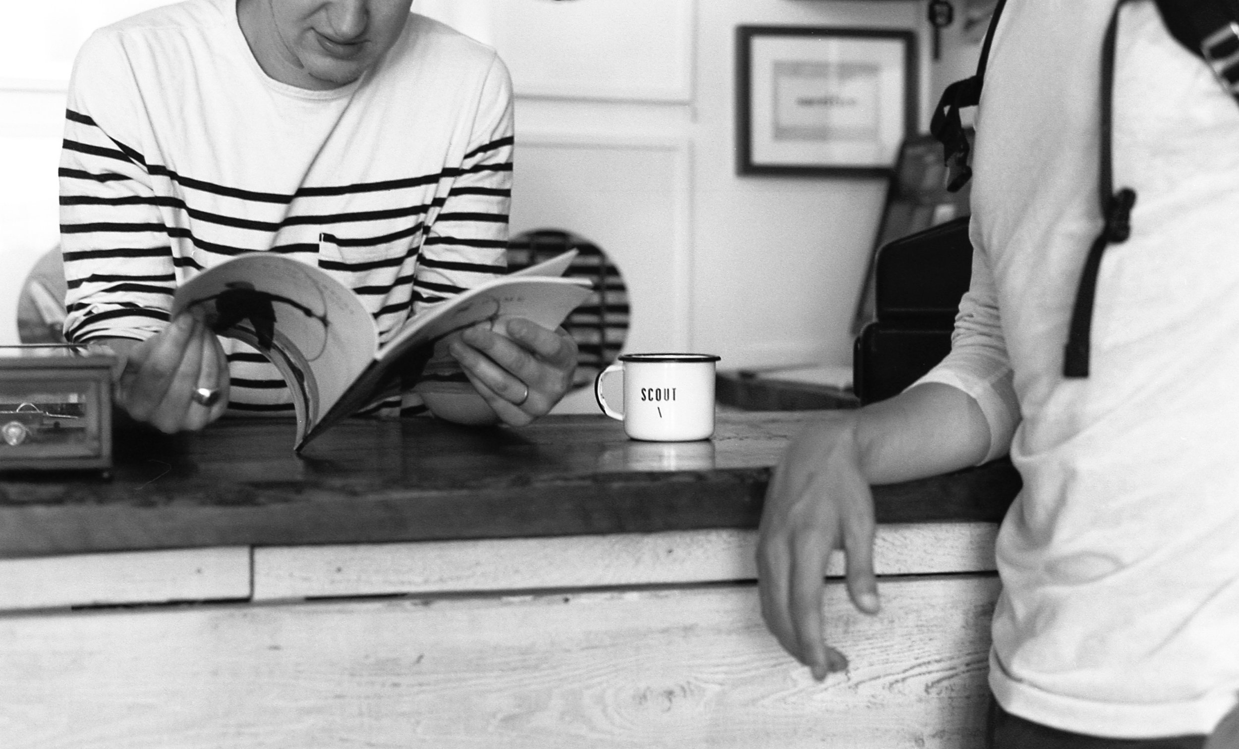 Two people lean on a counter, one reads a magazine