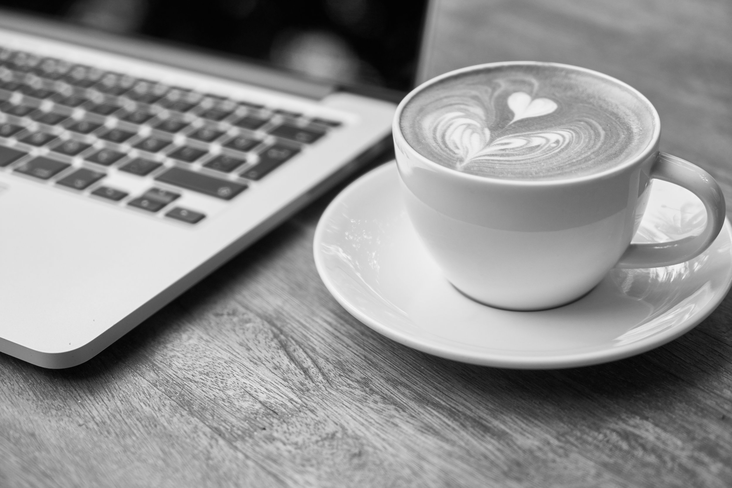 A latte and a Macbook sit on a wooden table