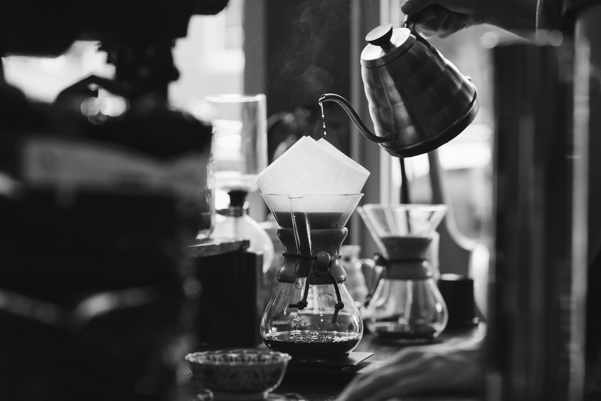 A barista pours hot water over grounds in a Chemex coffemaker in a cafe