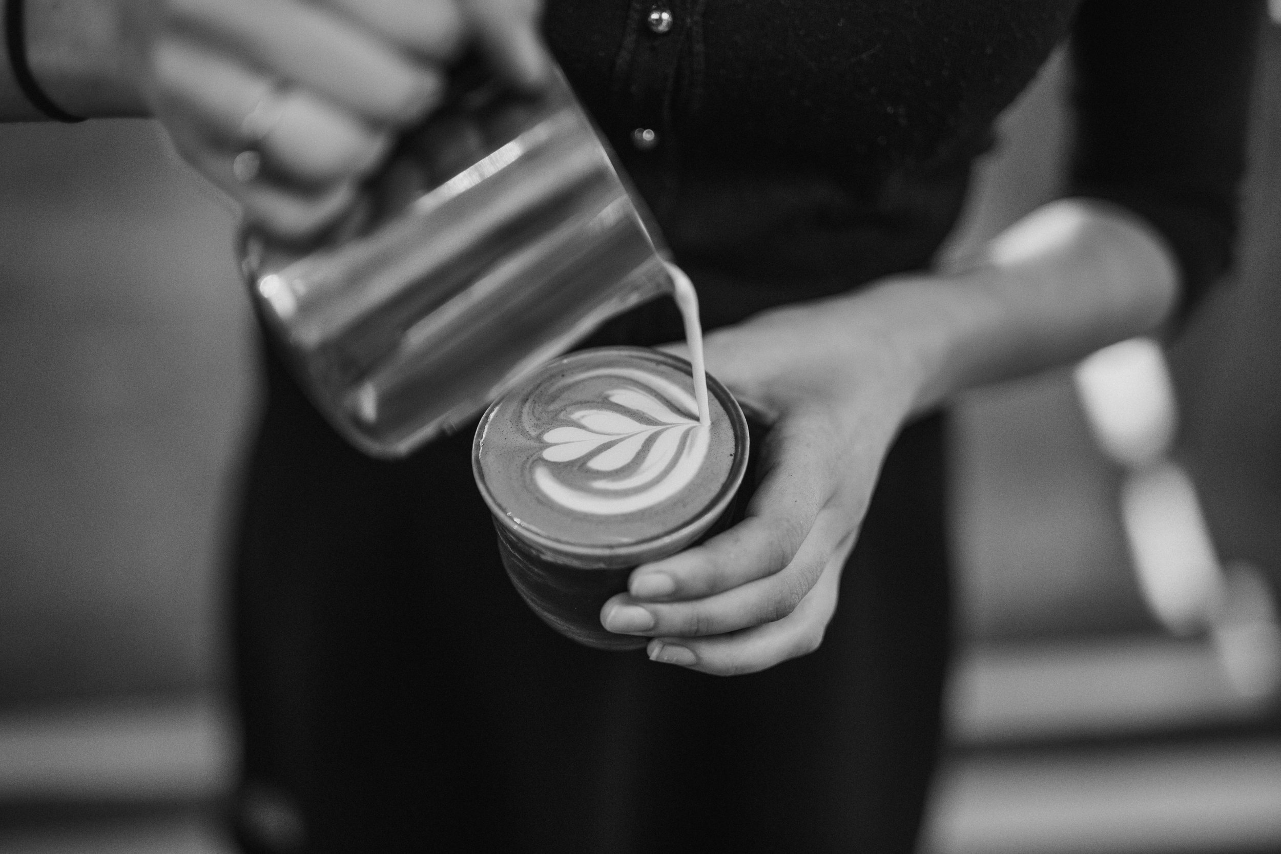 A barista pours a latte, seen from above.