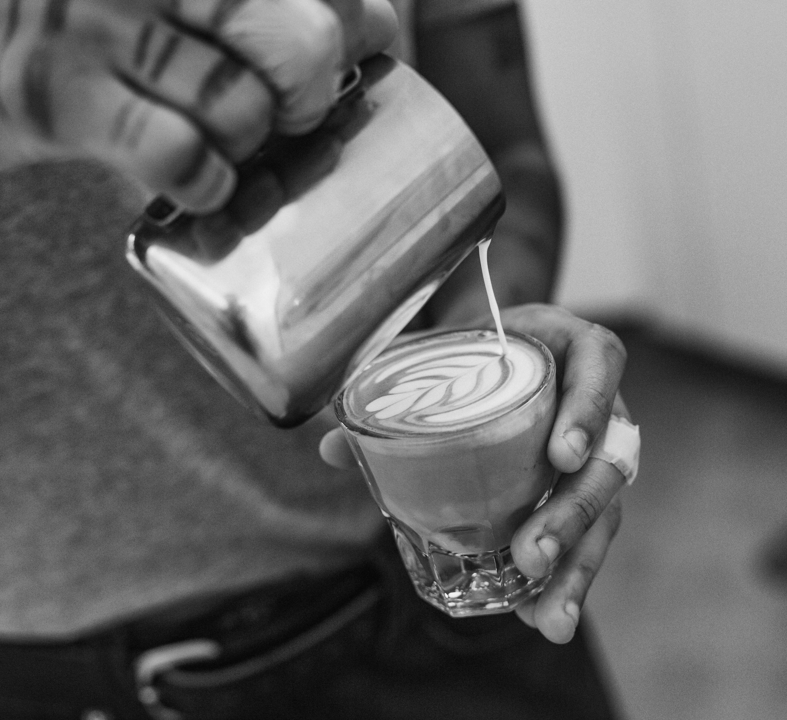 A barista pouring latte art into a cortado glass, possibly using non-dairy milk.