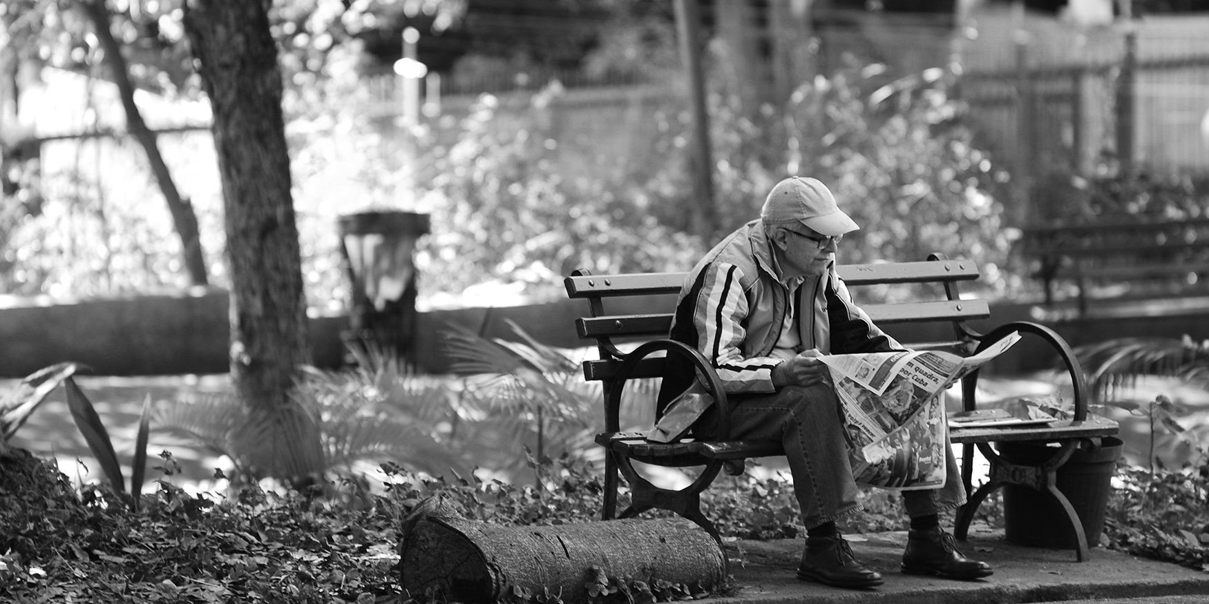 A man sits on a park bench reading a newspaper