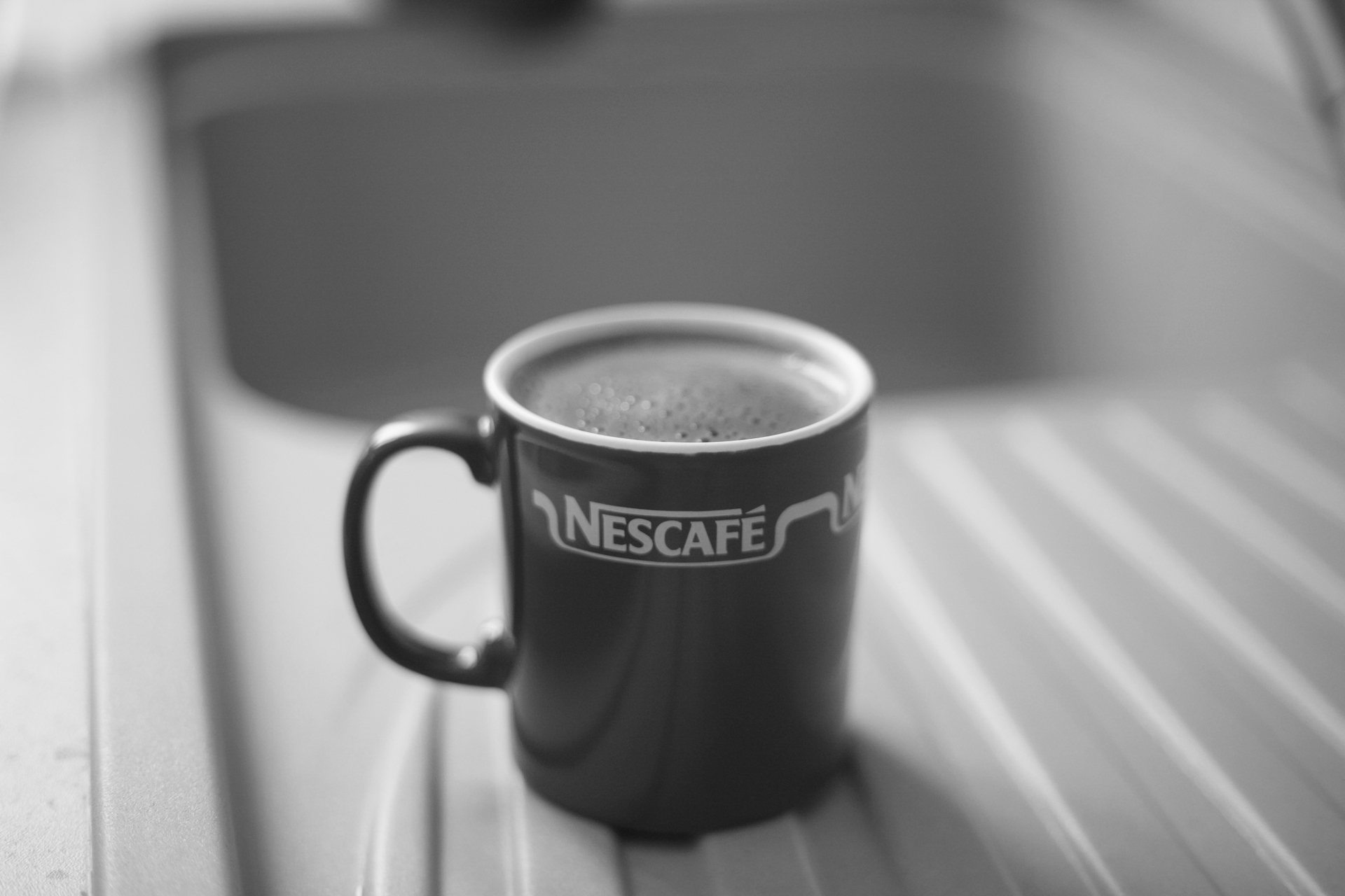 A coffee cup with “Nescafe” emblazoned on it sits next to a sink.