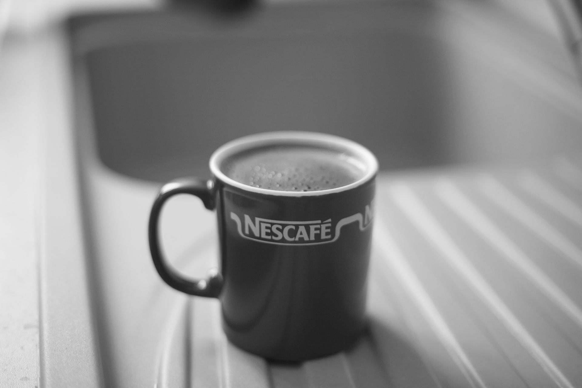 A cup of Nescafe coffee sits beside a sink
