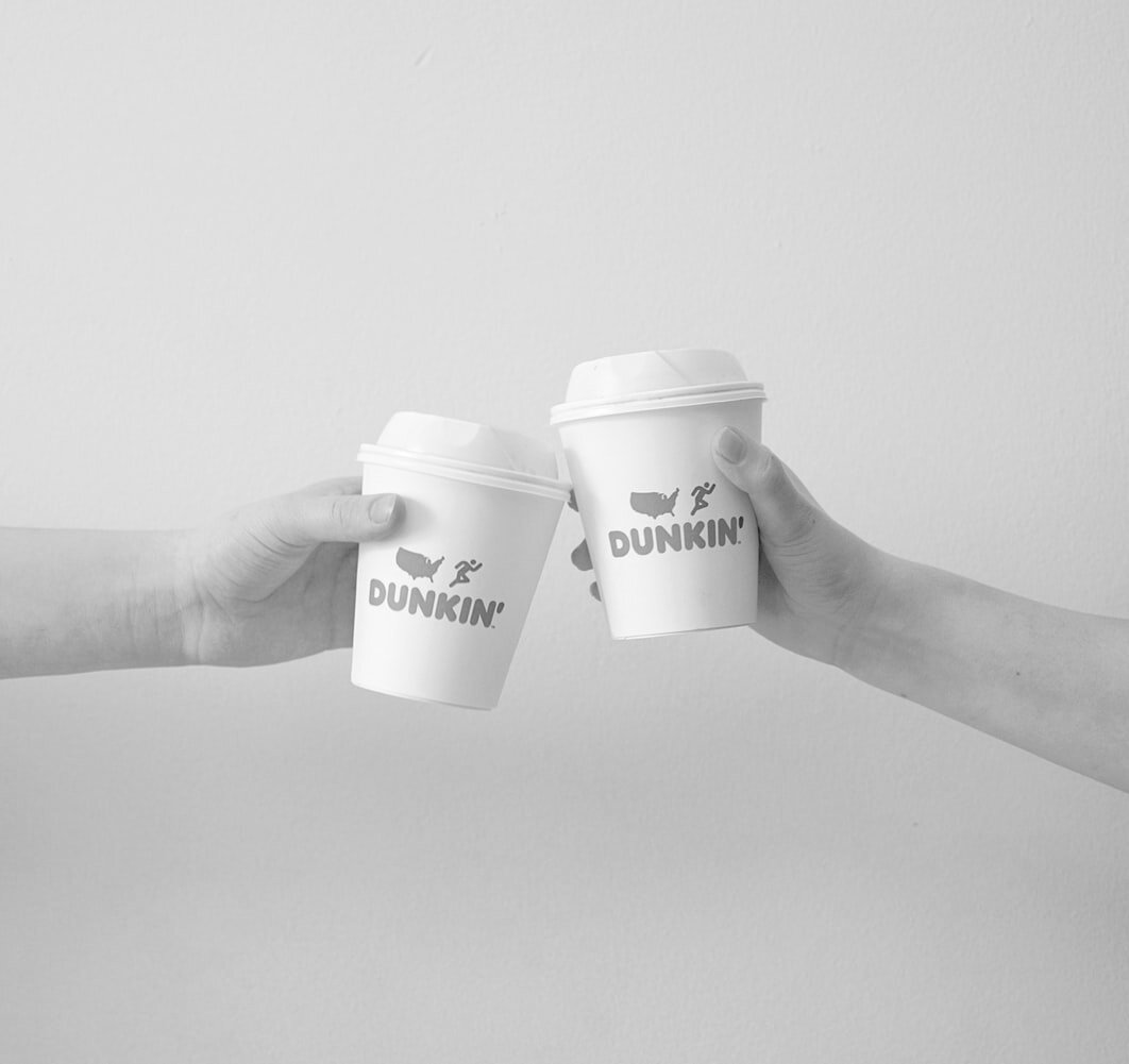 Two hands holding paper Dunkin coffee cups