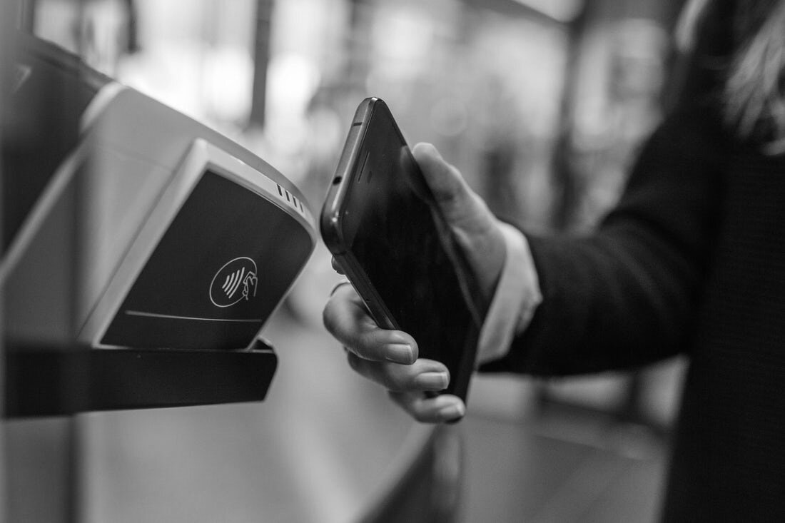 A hand holds a smartphone up to a mobile pay machine