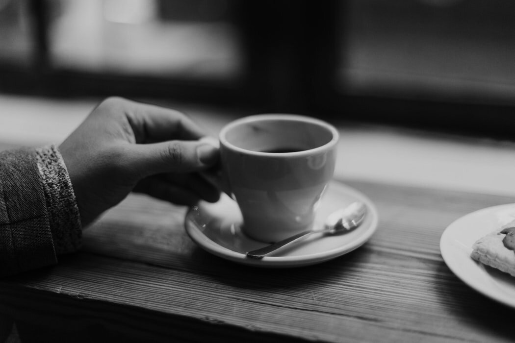 A hand holds an espresso cup on a saucer