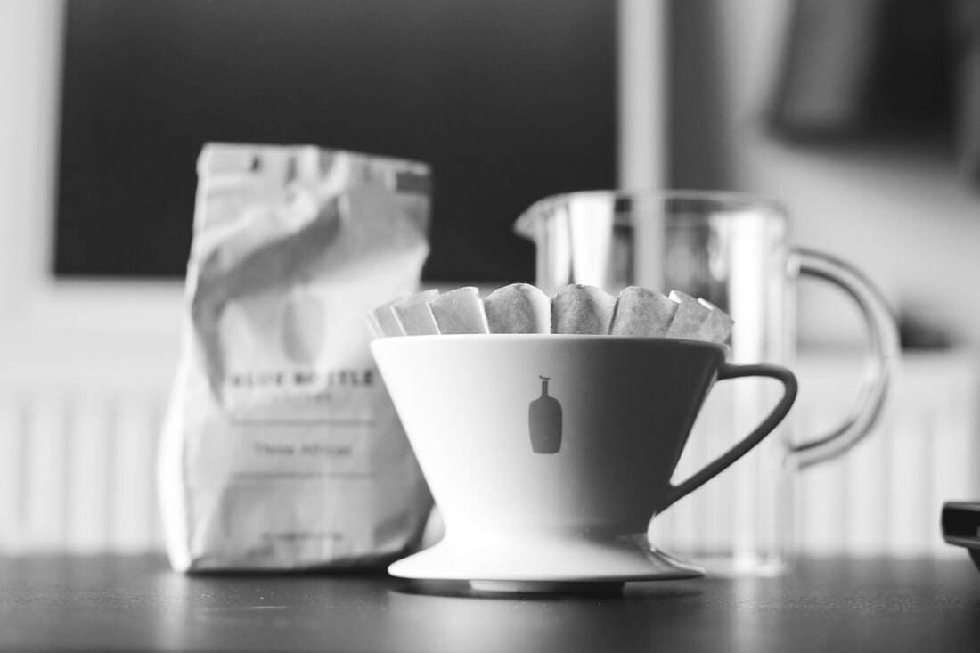 A Blue Bottle coffee dripper with filter and a bag of coffee in the background