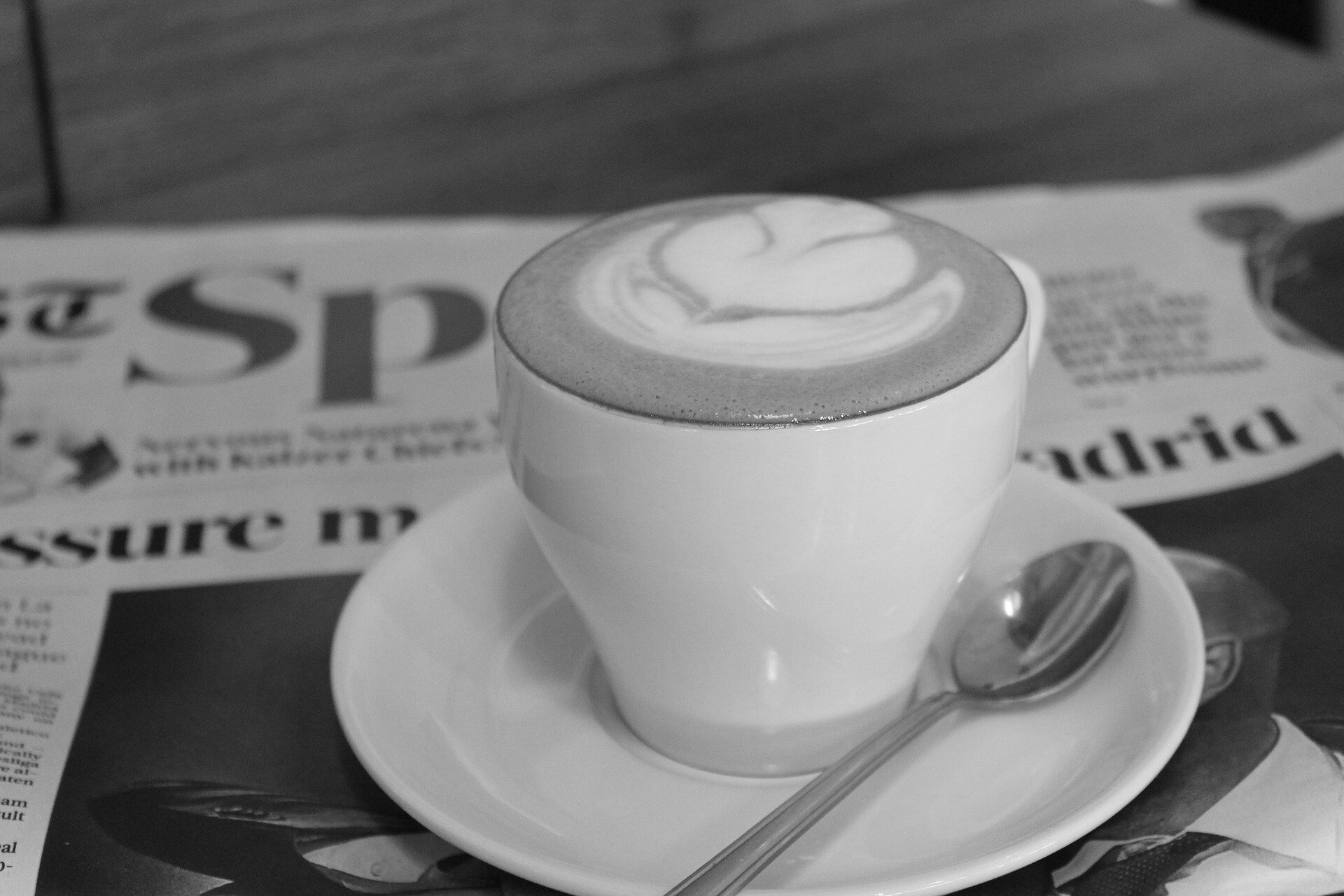A macchiato cup with latte art sits atop a newspaper on a table