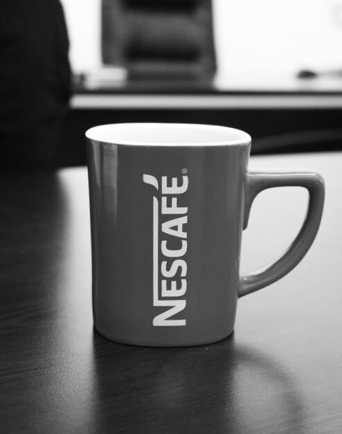 A mug with Nescafe written on the side sits on a table