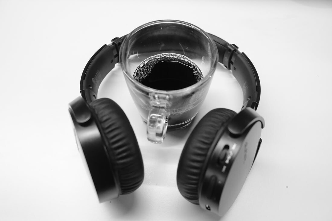 A pair of black headphones lay on a table around a glass of coffee.