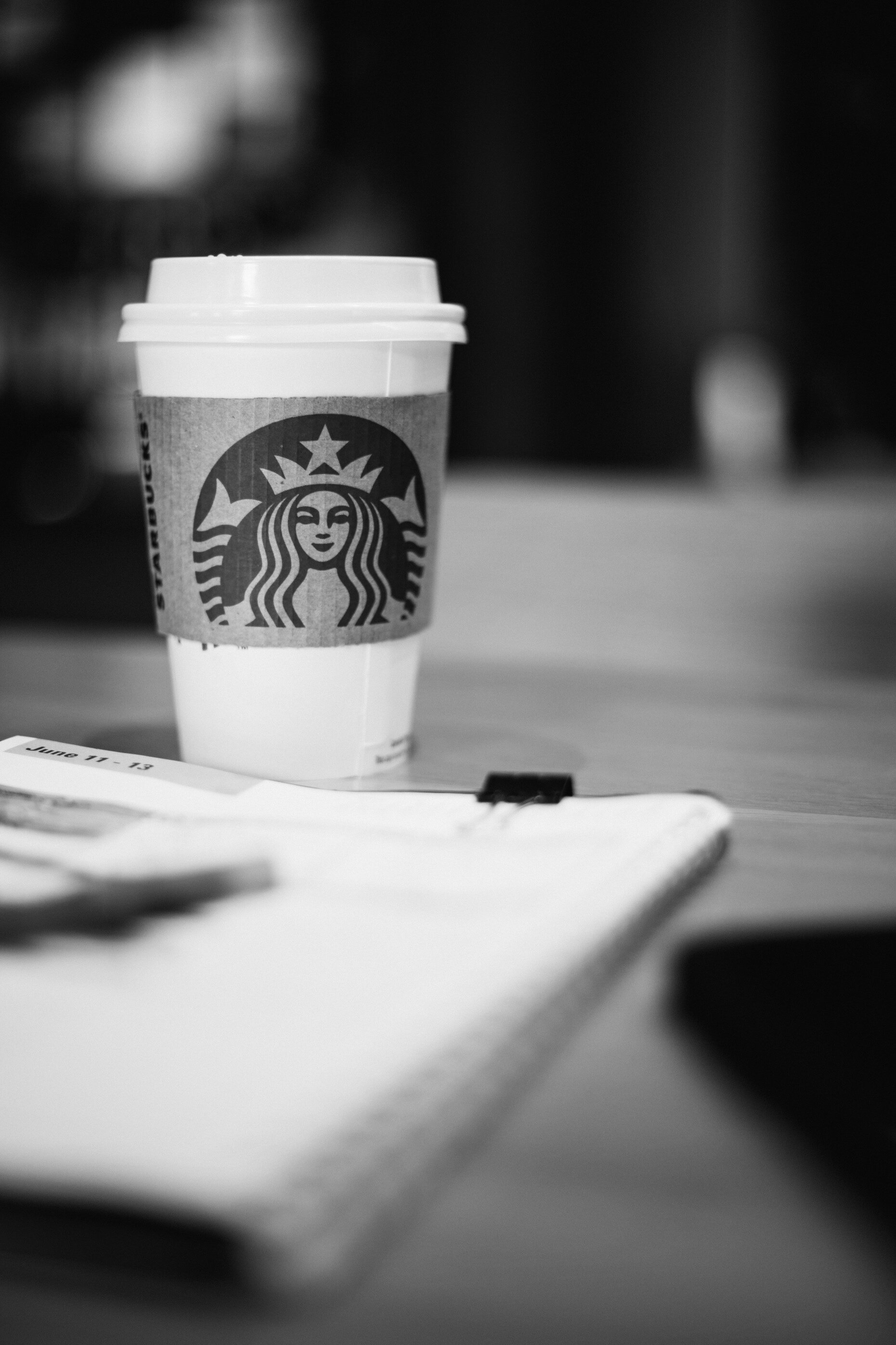 A white Starbucks disposable coffee cup with cardboard sleeve sits on a table