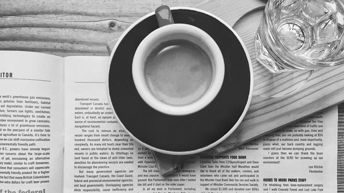 An espresso cup sits on a wooden tray atop an open magazine, seen from above.