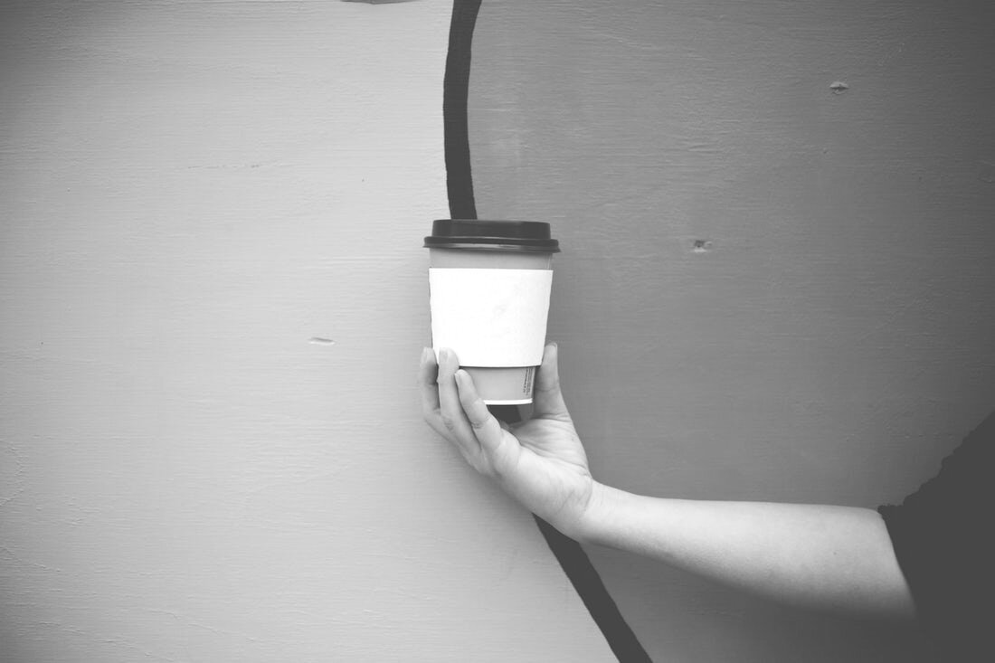 A hand holds a disposable coffee cup in front of a painted wall
