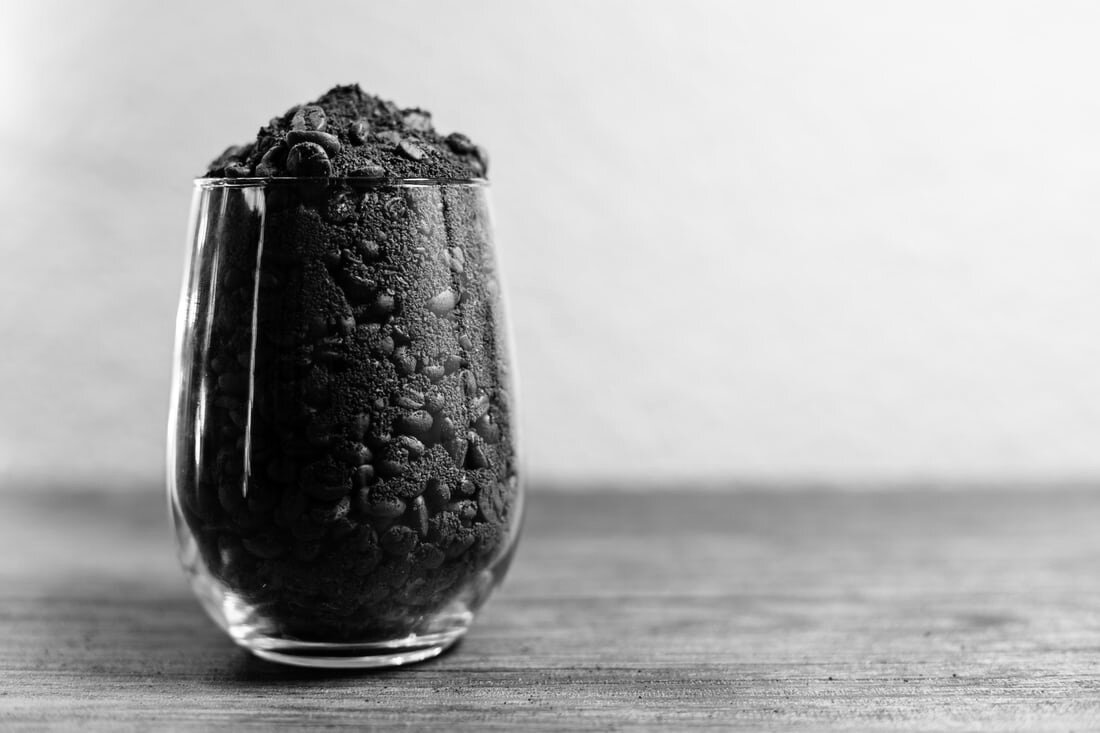 A glass full of ground coffee and beans sits on a wooden table. Via Unsplash