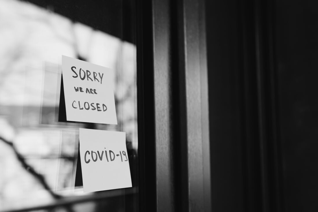 Post-it notes on a glass door read “SORRY WE ARE CLOSED” and “COVID-19”. Via Unsplash