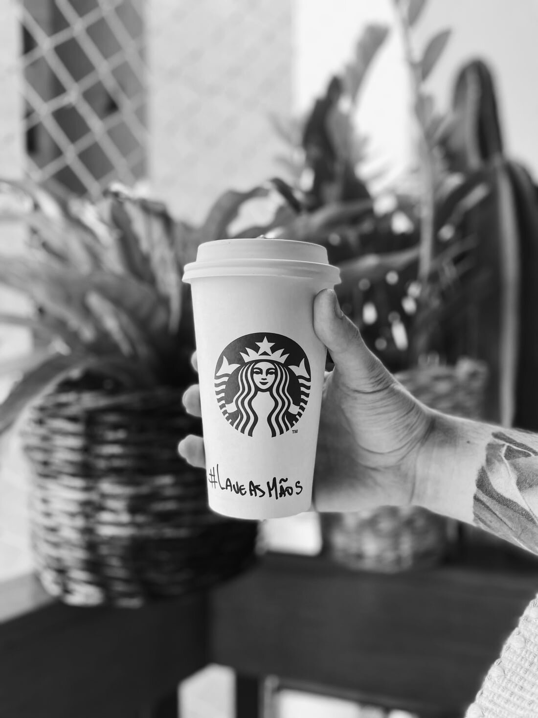 A hand holds up a white Starbucks cup with “LAVE AS MAOS” written on it. Via Unsplash.