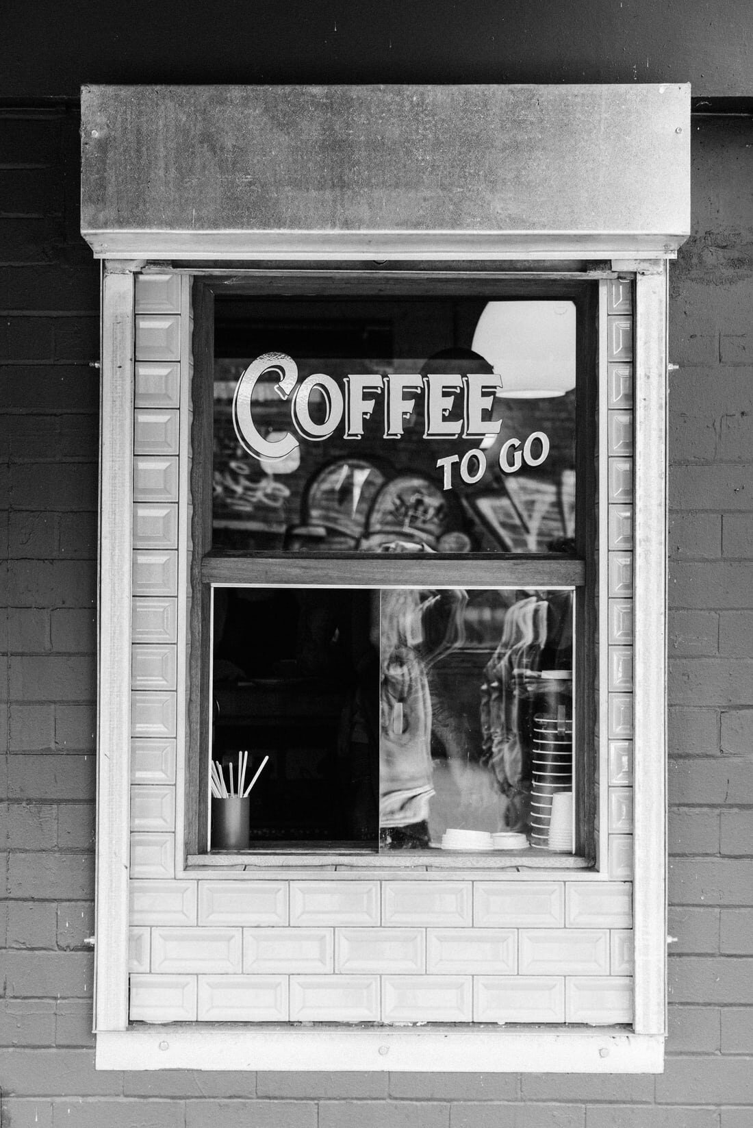 A takeout window with a sign reading “COFFEE TO GO” set within a brick wall. Via Unsplash