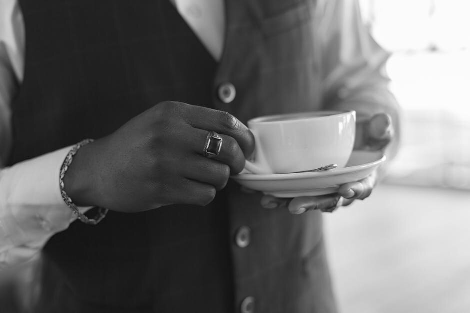 A person wearing a ring holds a white cup of coffee in closeup. Via Pexels.