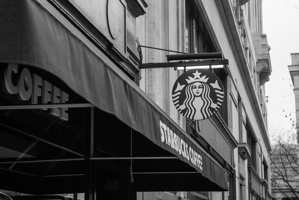 A Starbucks sign hangs above a cafe awning. Via Pexels