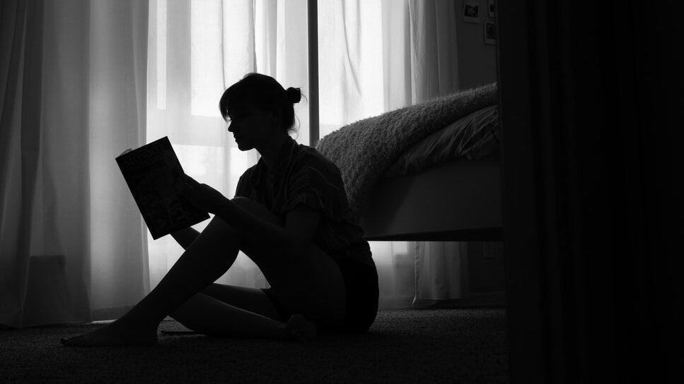 A person sits on the floor reading a book.&nbsp;via Unsplash