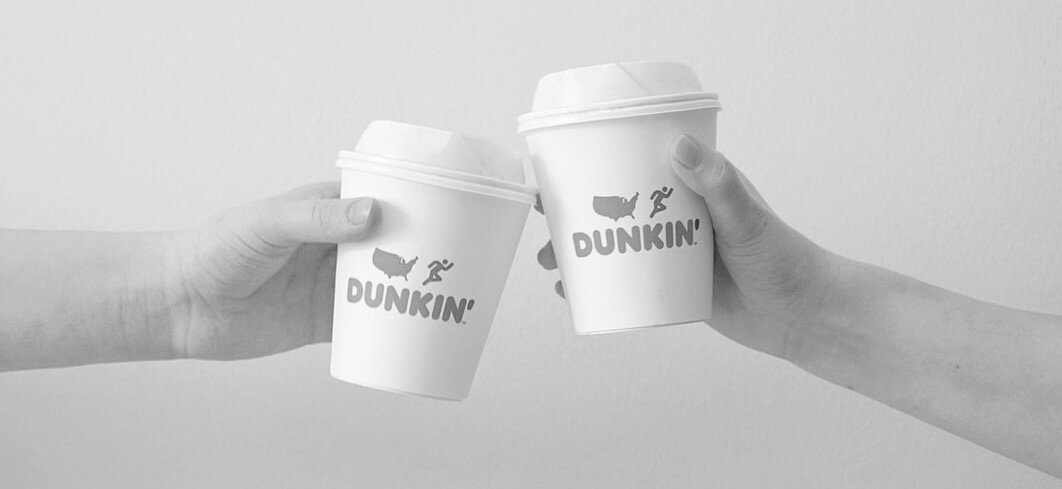Two hands cheersing with Dunkin’ coffee cups. Via Unsplash