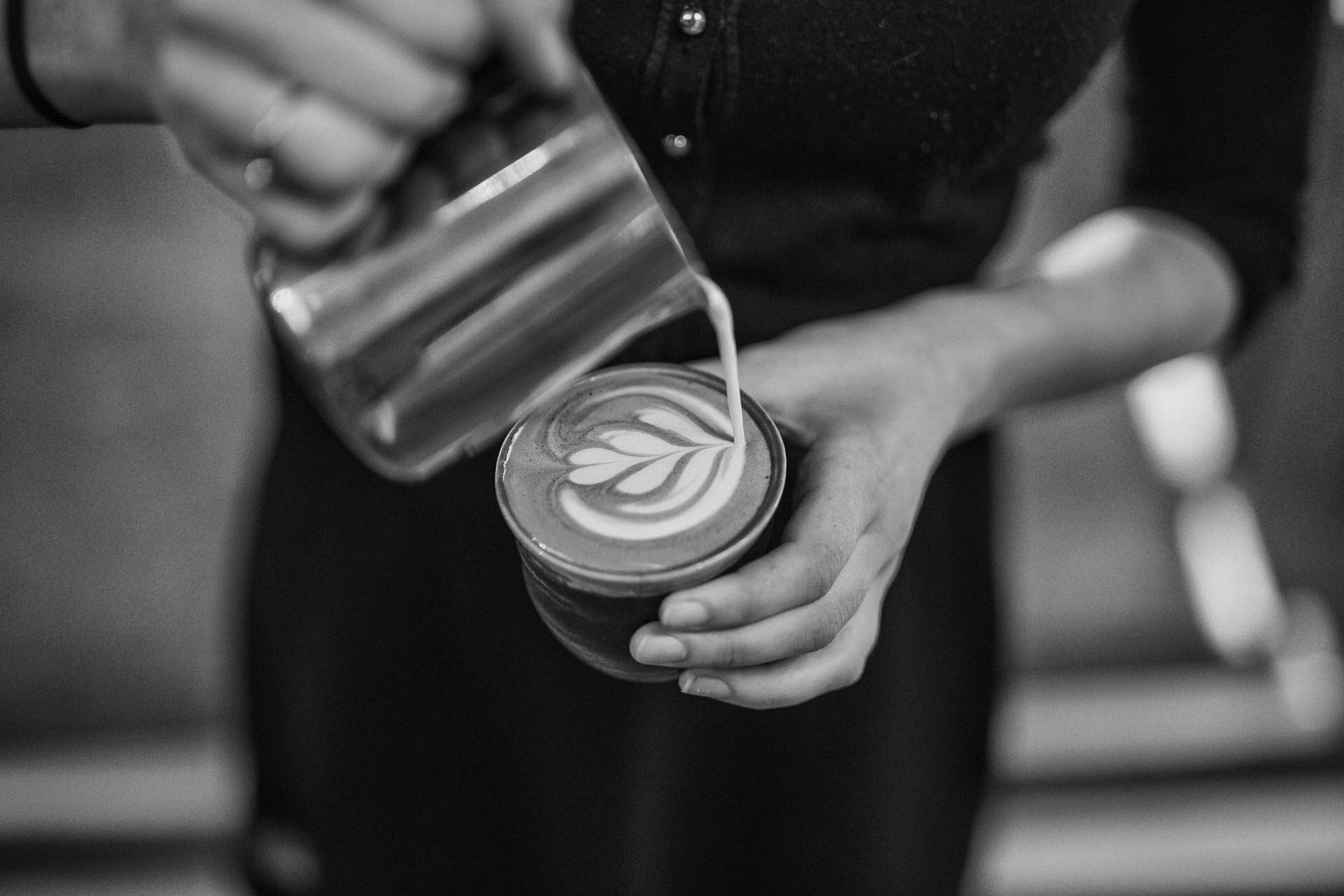 A barista pours latte art into a cup, seen from above. Via Unsplash.