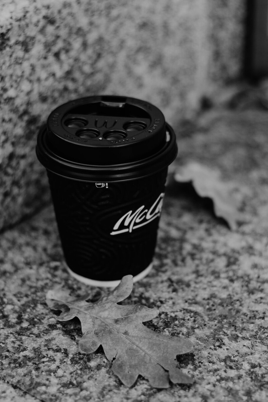 A McDonald’s takeaway coffee cup sits on a stone bench surrounded by leaves. Via Unsplash