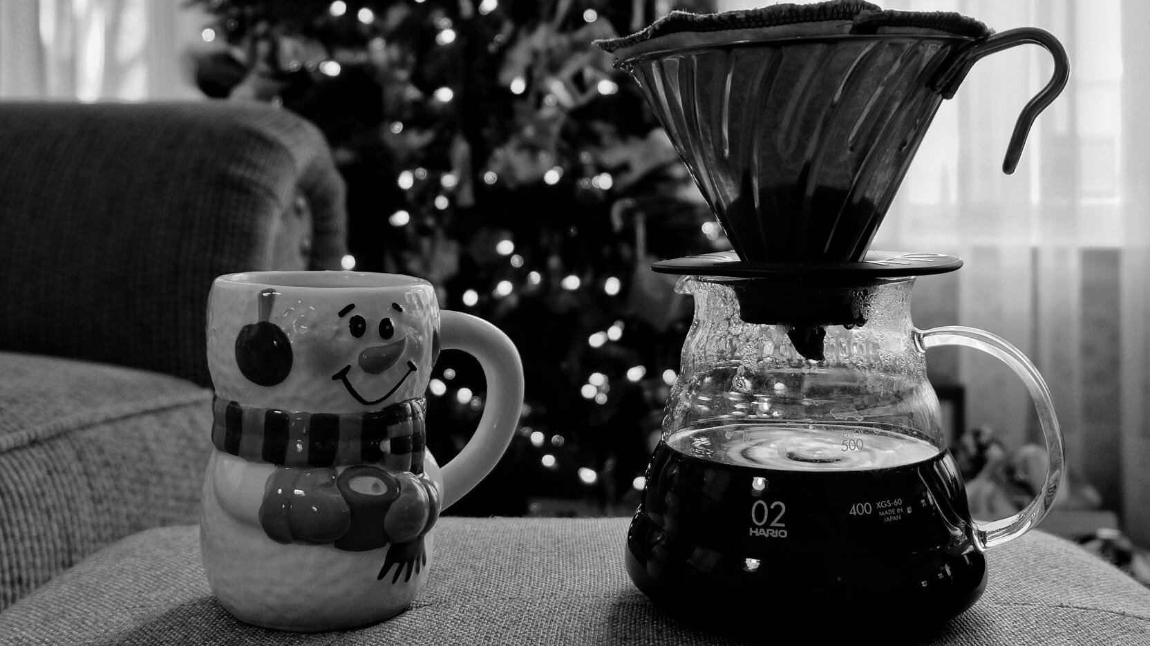 A snowman-themed mug and Hario V60 brewing device in close up in front of a Christmas tree