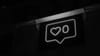 A neon sign of an Instagram like button against a black background