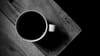 A cup of black coffee on the edge of a wooden table, seen from above