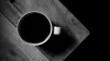 A cup of black coffee on the edge of a wooden table, seen from above